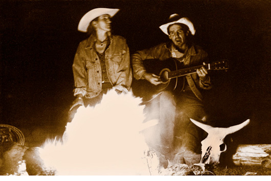 Two cowboys singing in front of the camp fire